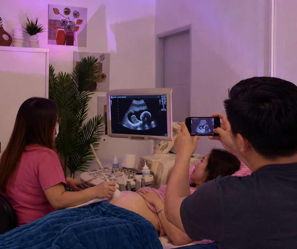 Pregnant patient undergoing an ultrasound while her partner photographs the 2D ultrasound monitor